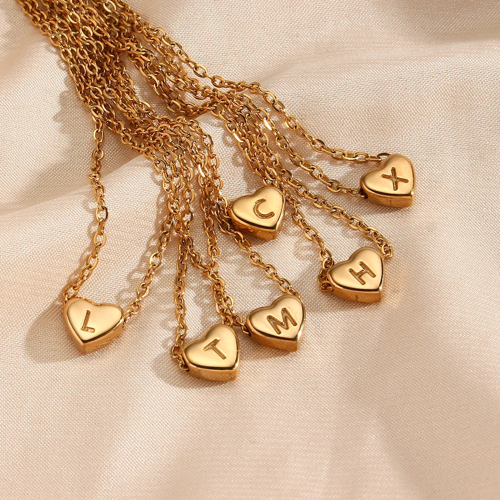 Gold necklaces with heart-shaped pendants displaying letters on a beige fabric background