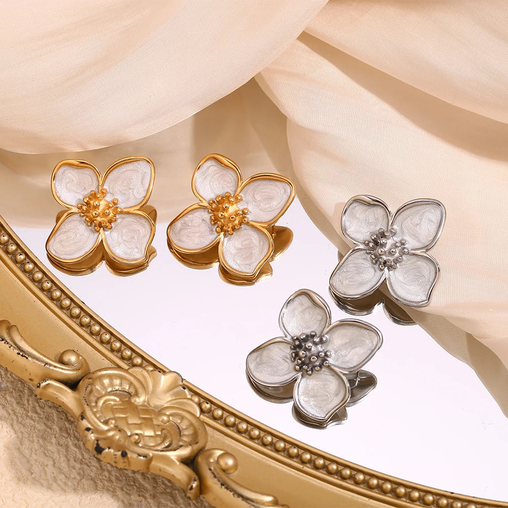 A pair of 18K gold coated floral earrings with white enamel petals displayed on a mirror
