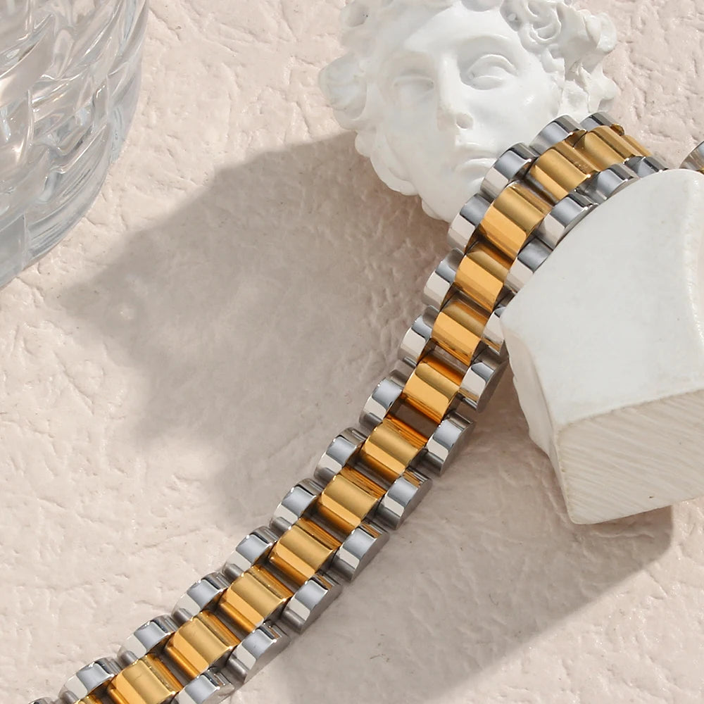 Metallic watch strap with gold and silver tones on a classical sculpture head in the background.