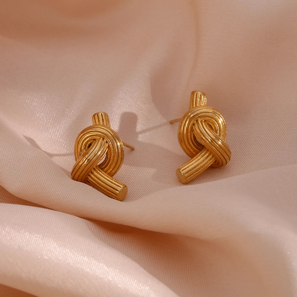 A pair of 18K gold plated stainless steel knot earrings with a textured surface.