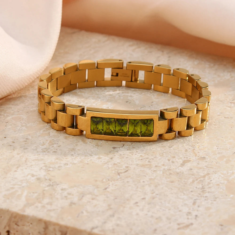 Gold link bracelet with green gemstones on a beige surface