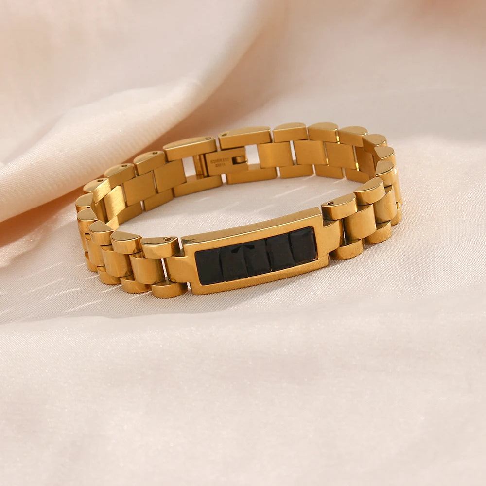 Gold steel bracelet with a black rectangular tag on a beige background