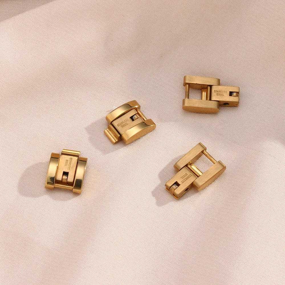 Four gold extender clasps on a light pink fabric background