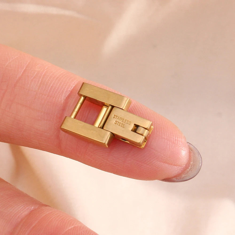 Gold bracelet link clasp on a finger against a neutral background