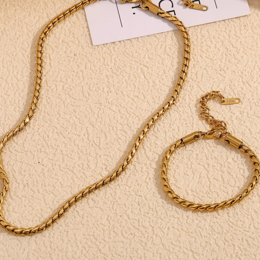 A stainless steel twisted chain necklace, displayed on a textured beige background.