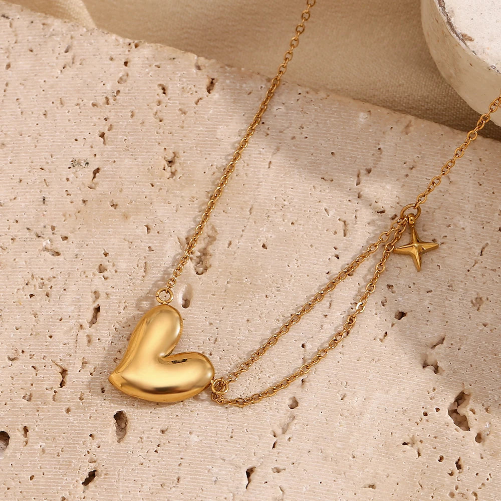 A gold steel necklace with a heart-shaped pendant and a small star charm