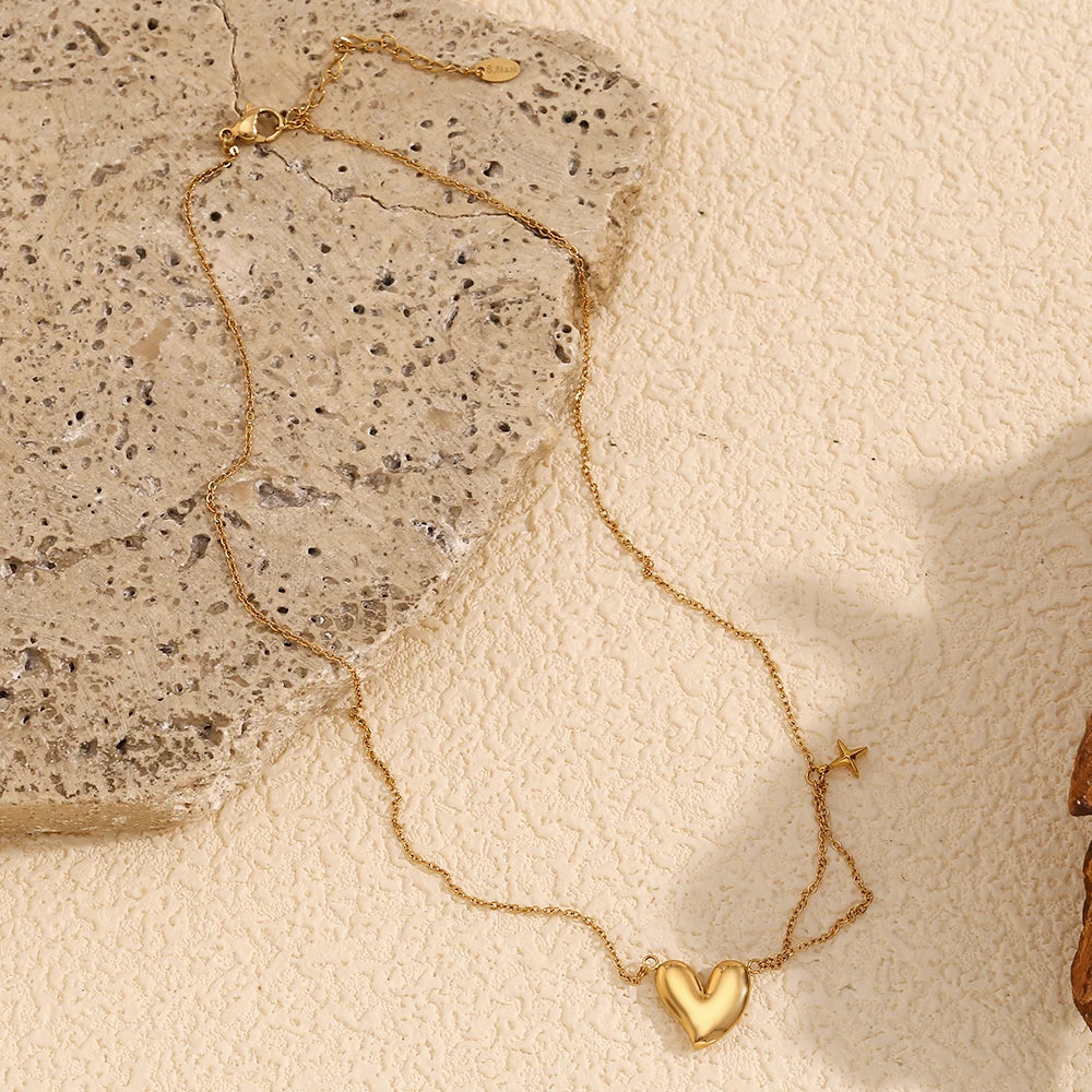 A gold steel necklace with a heart-shaped pendant and a small star charm