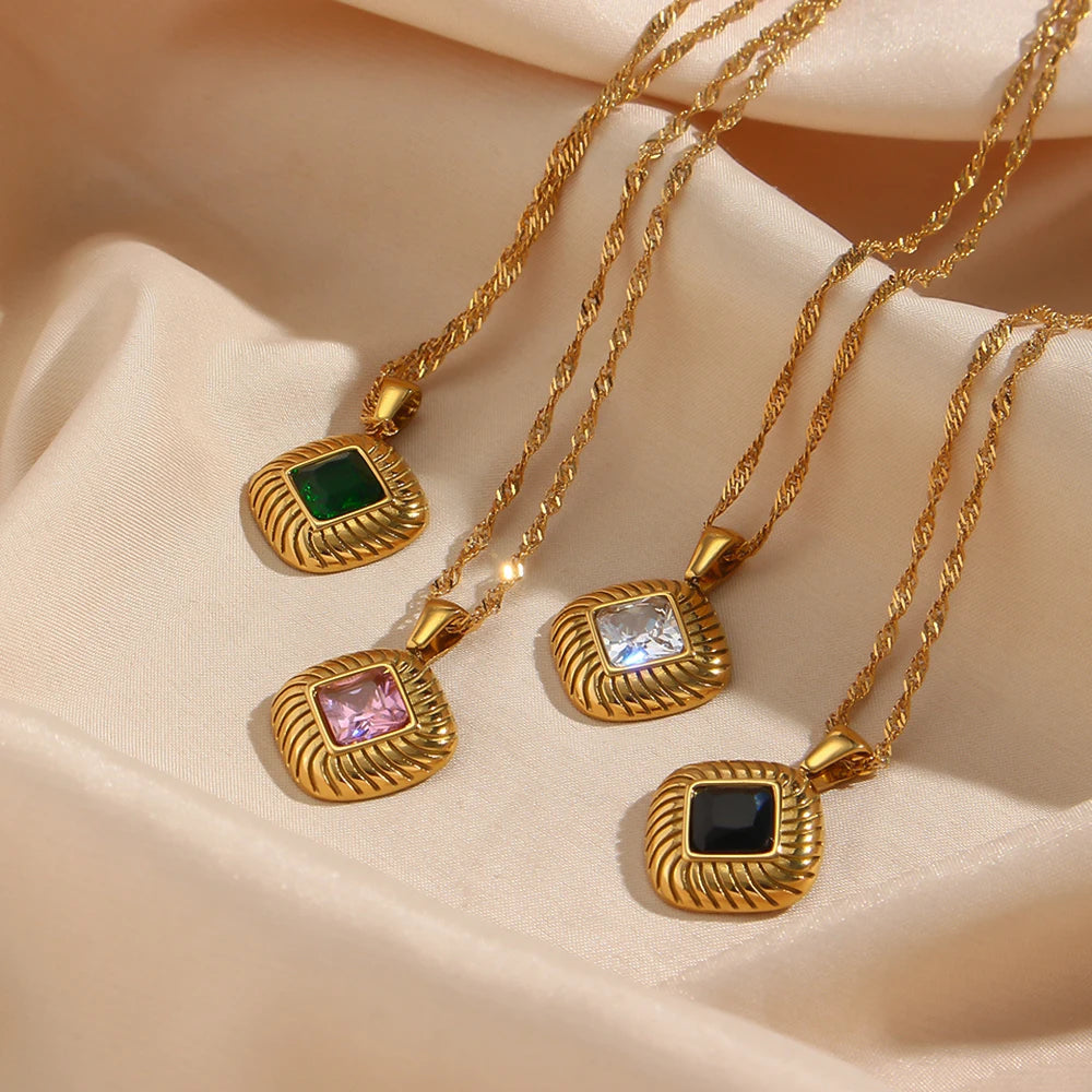 Gold-plated stainless steel necklaces with a square pendant featuring a center crystal, on a beige fabric.
