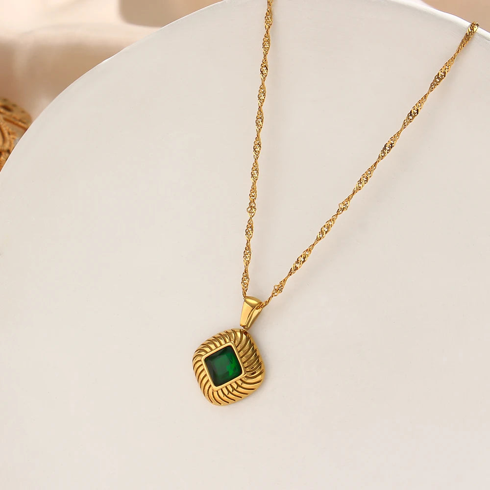 A gold-plated stainless steel necklace with a square pendant featuring a green crystal, on a white background.