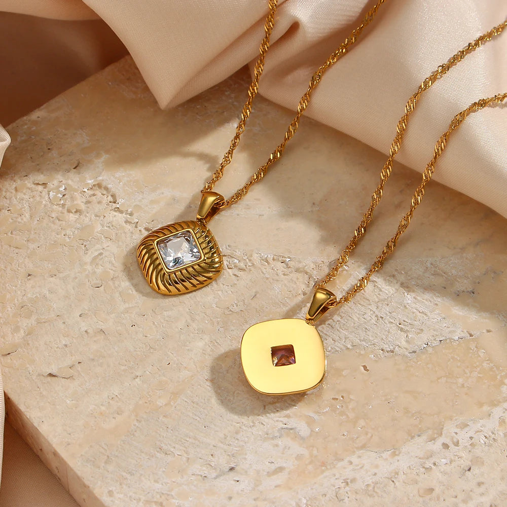 A gold stainless steel necklace with a square pendant featuring a crystal, photographed from the front and the back, on a beige textured background.