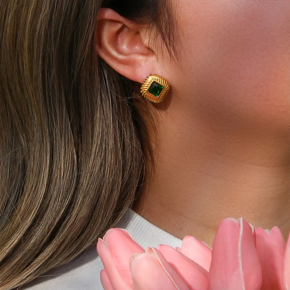 A pair of stainless steel stud earrings with a geometric design and a central clear crystal, displayed in a woman's ear.