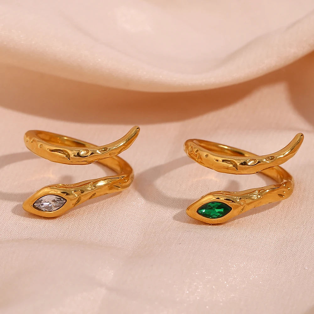Two gold-colored rings with a textured design and a green gemstone, displayed against a beige fabric background