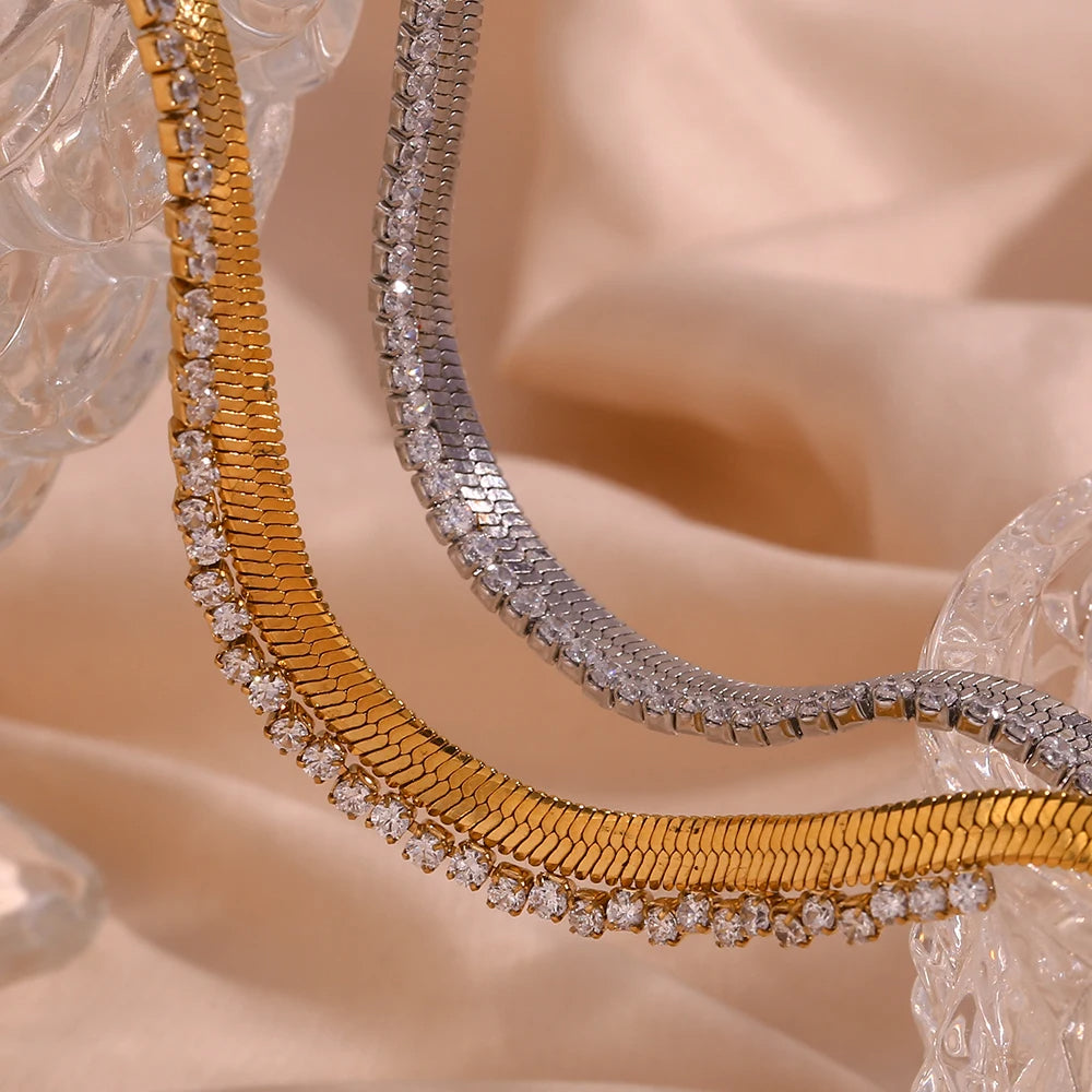 Two gold and silver necklaces with diamond accents on a beige fabric background
