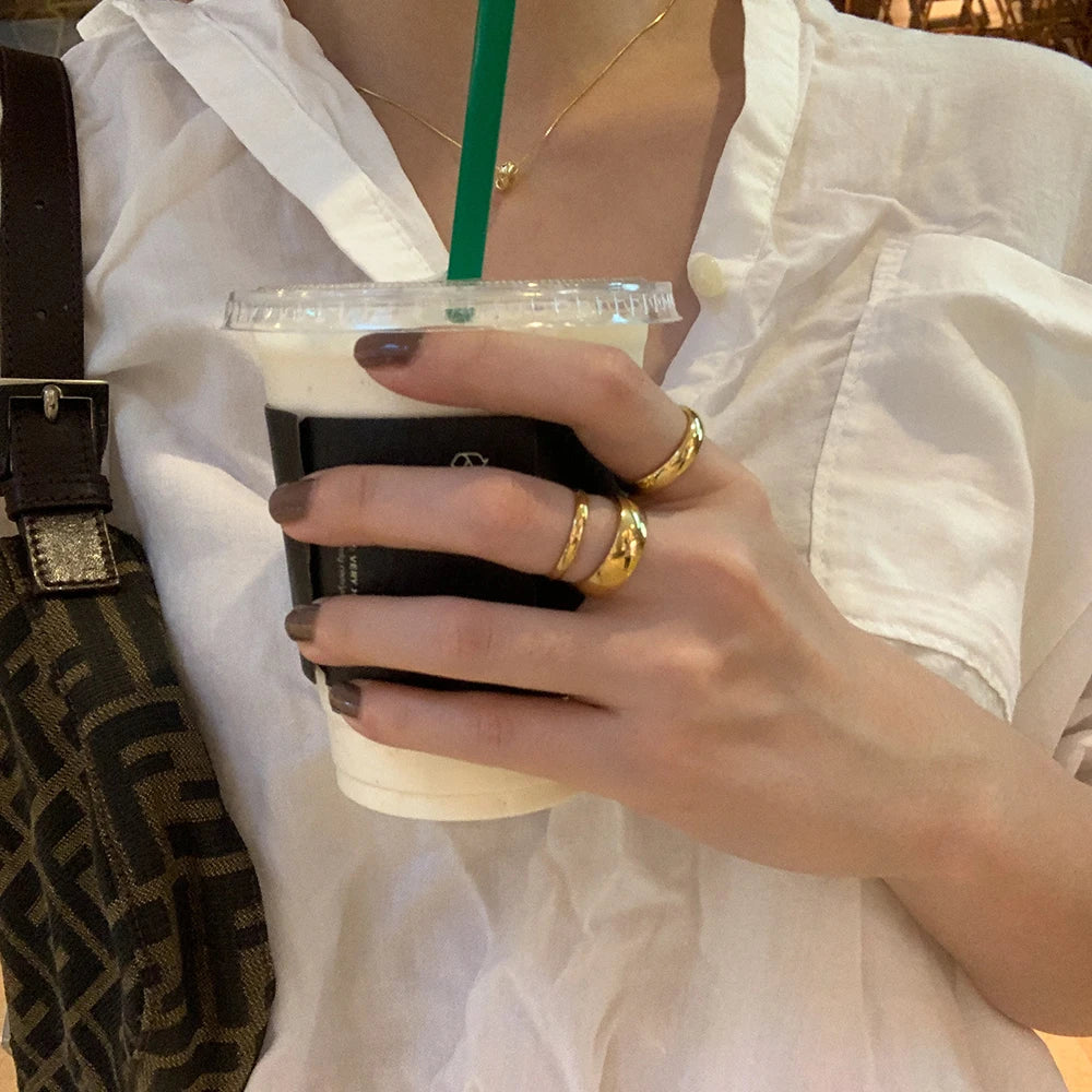 Person holding a matcha drink with a white shirt and gold rings.
