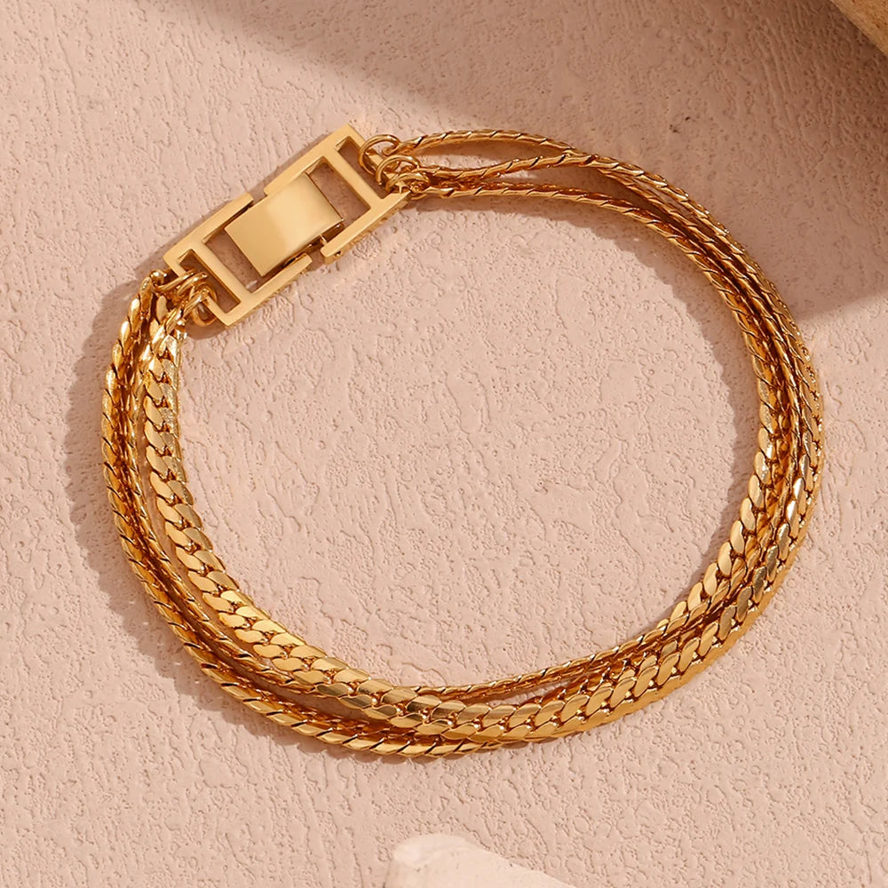 A gold stainless steel bracelet with a triple chain design, featuring a clasp closure.