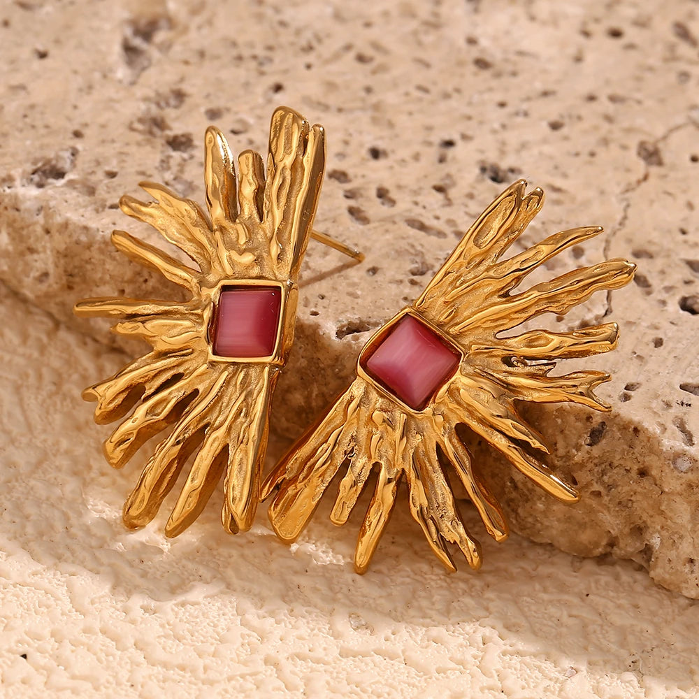 A pair of gold-colored earrings designed to resemble sun rays with a square pink gem at the top.