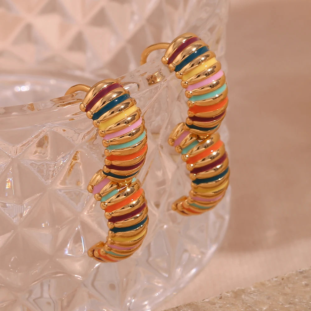 Colorful hoop earrings with gold accents hanging from a glass