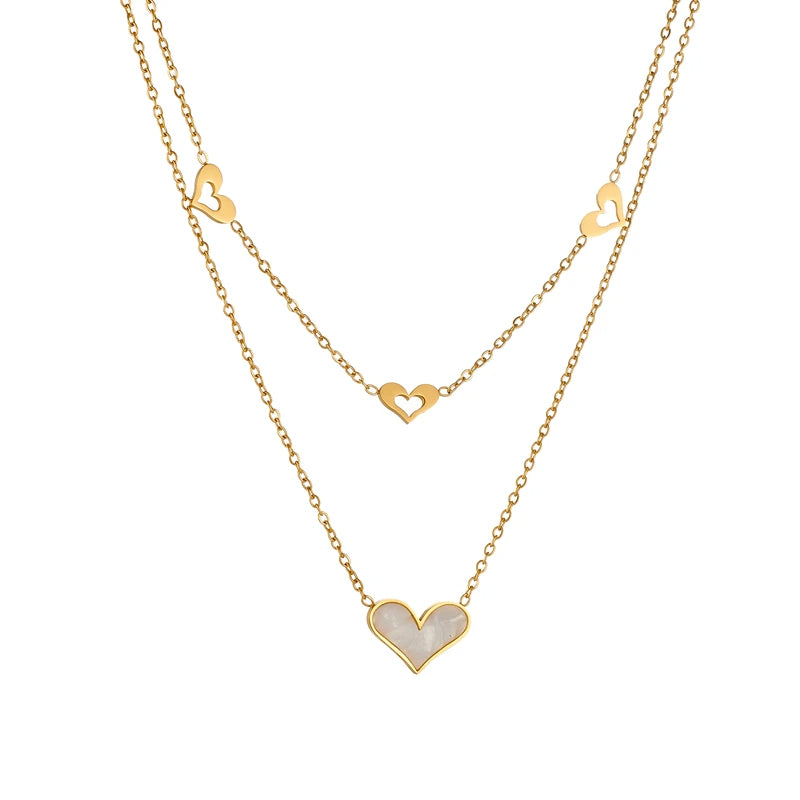 A double layered necklace with gold chains and heart-shaped pendants, one of which is made from a natural shell