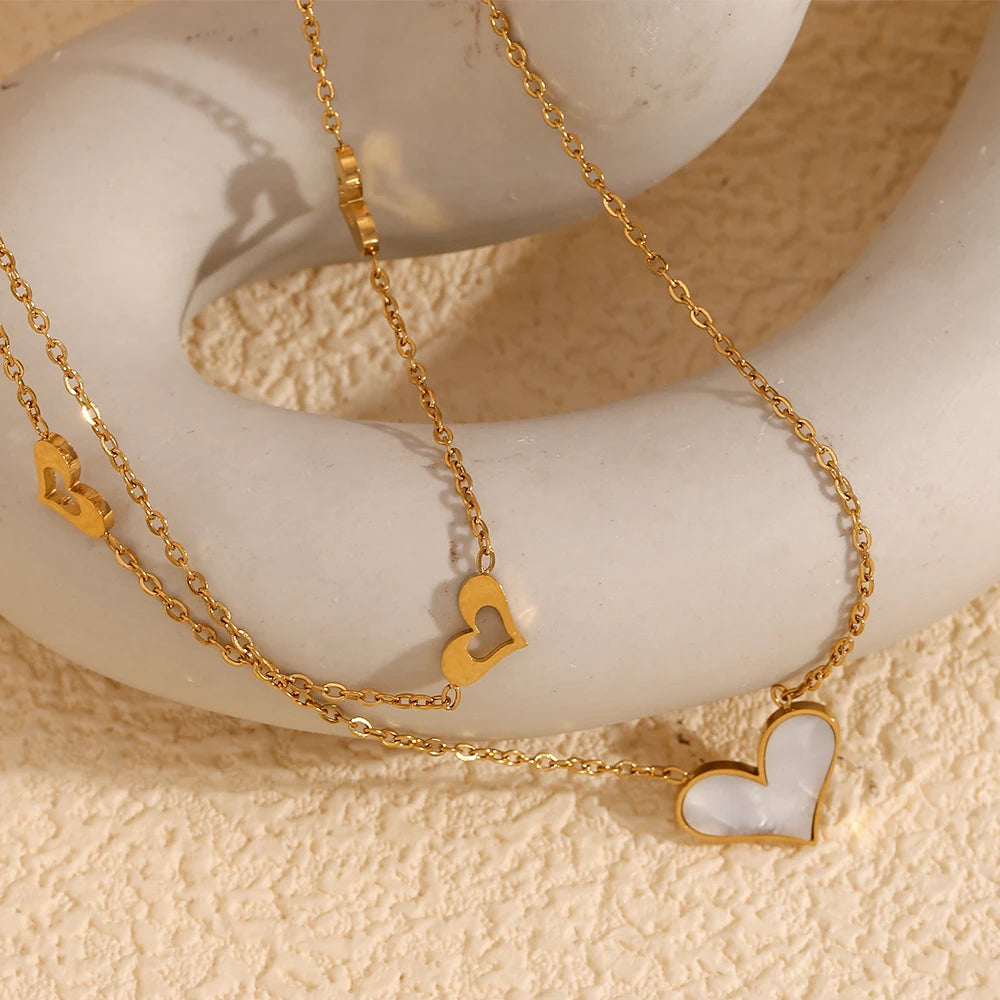 A double layered necklace with gold chains and heart-shaped pendants, one of which is made from a natural shell
