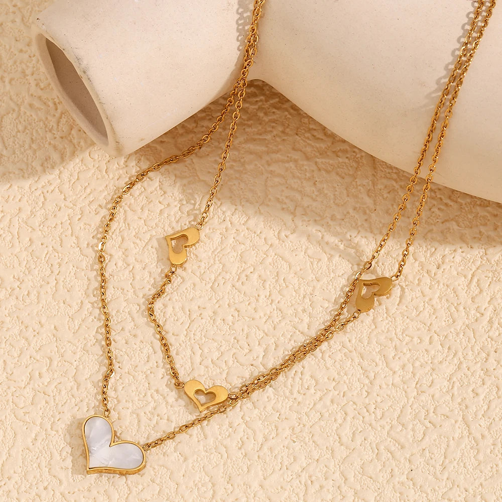 A double layered necklace with gold chains and heart-shaped pendants, one of which is made from a natural shell