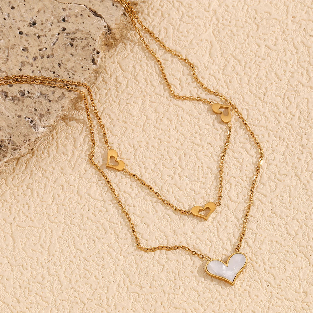 A double layered necklace with gold chains and heart-shaped pendants, one of which is made from a natural shell
