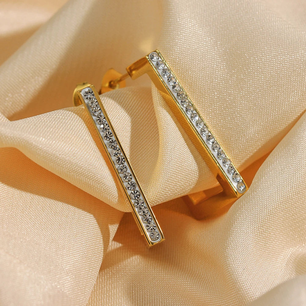 Gold earrings with clear stones on a beige fabric background