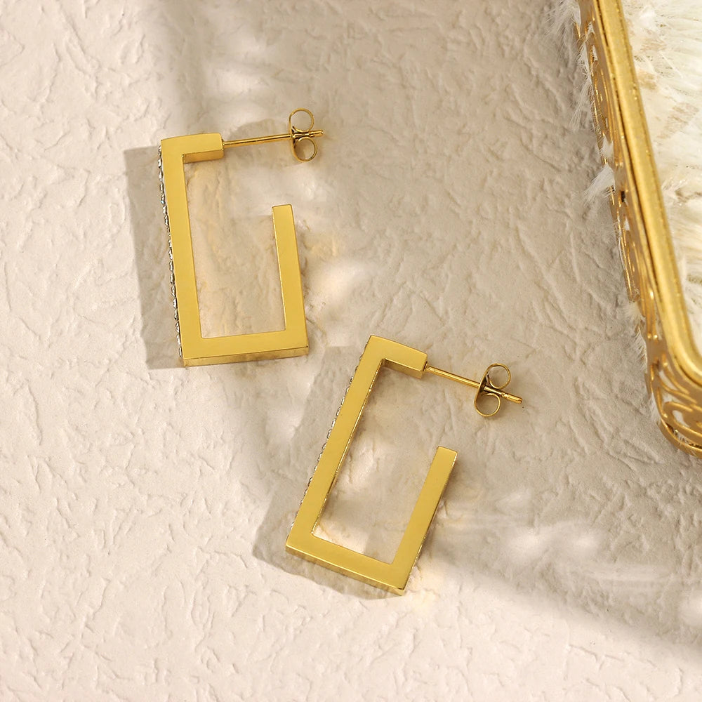 Gold squire hoop earrings on a textured beige surface