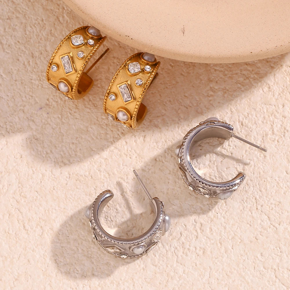 Gold and silver hoop earrings on a textured beige surface