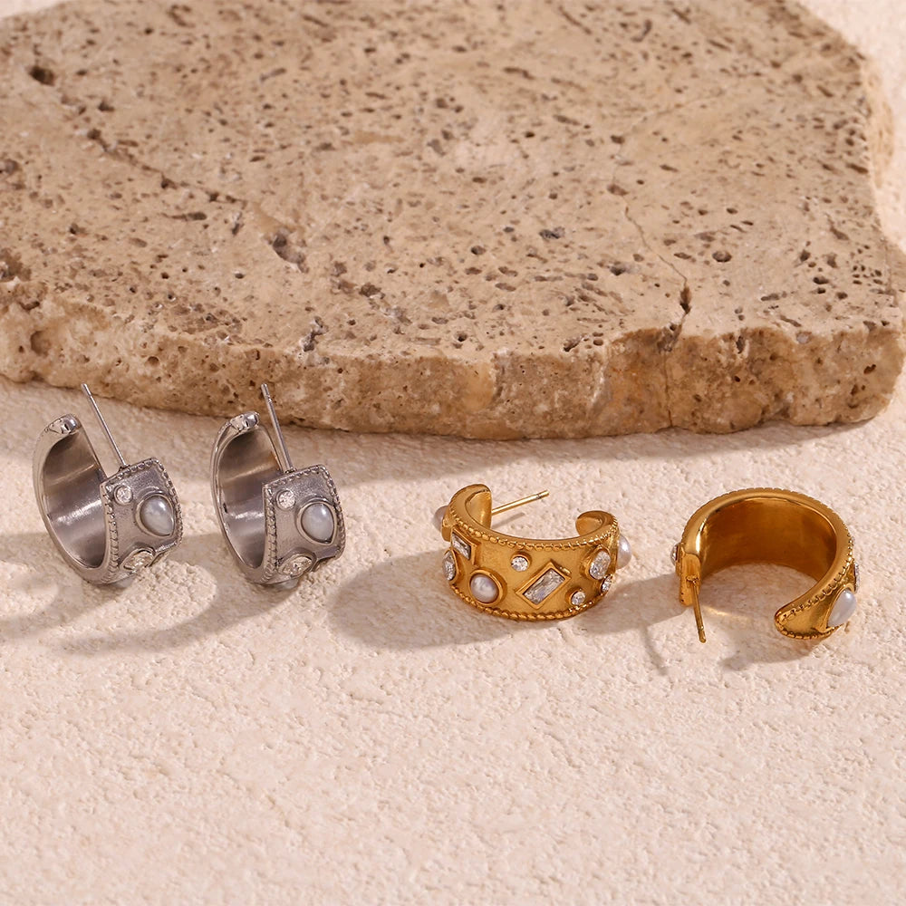 Two pairs of earrings, one silver and one gold, on a textured stone surface.