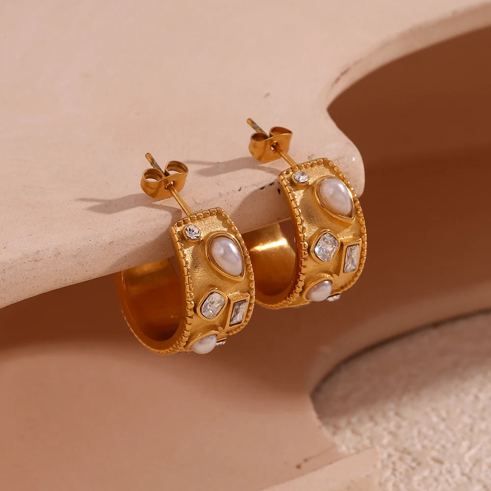 Gold hoop earrings with gemstone accents on a beige surface