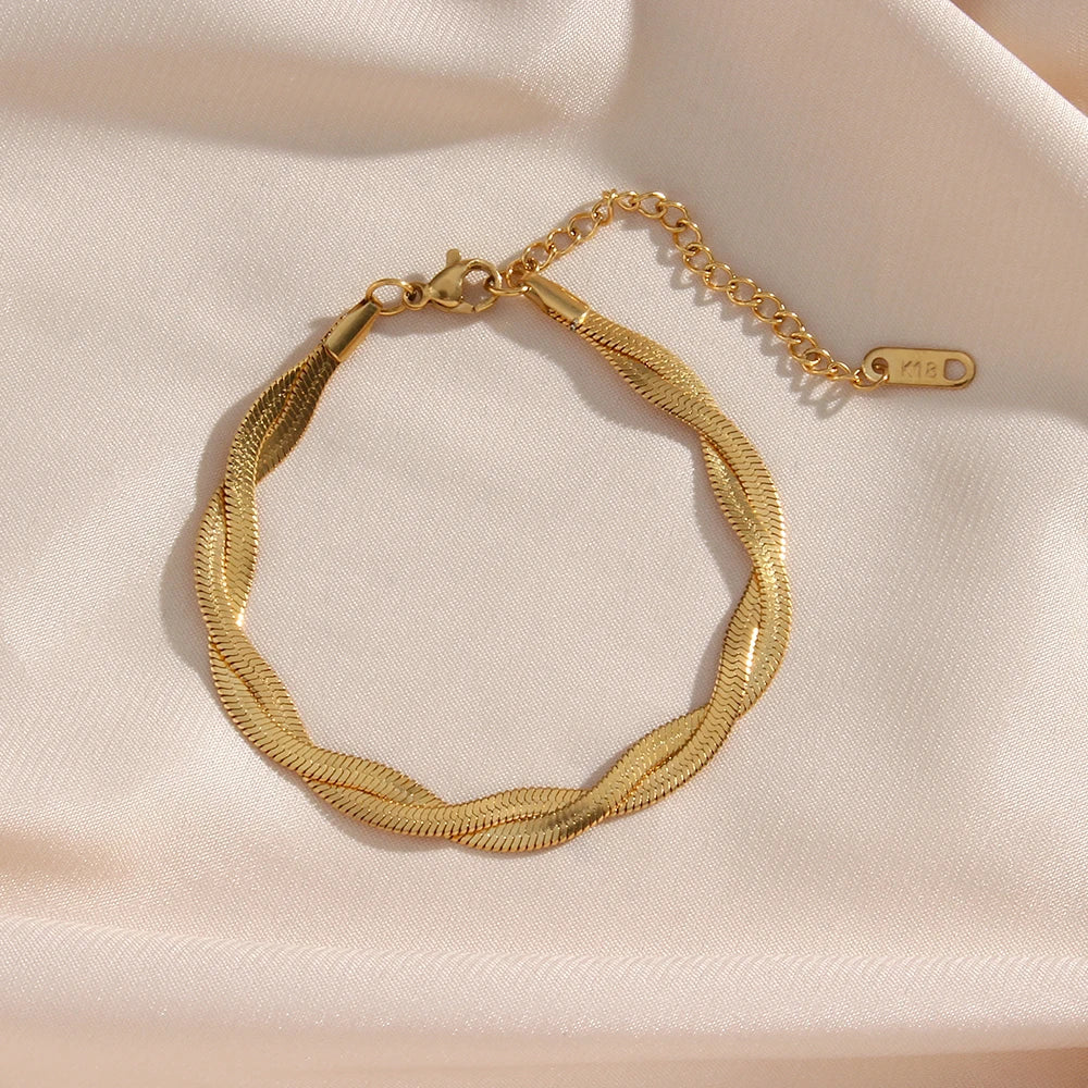 A gold twisted snake chain bracelet flat layed on a fabric background.