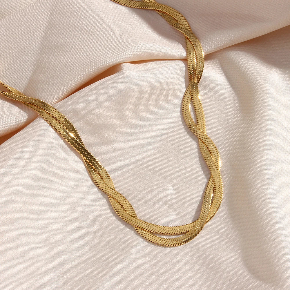 A gold twisted snake chain Necklace made from 18K gold plated stainless steel, flat layed on a fabric background.
