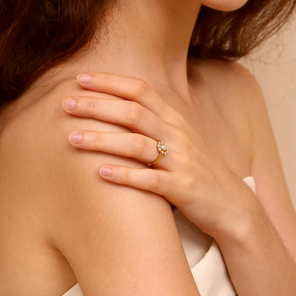 Close-up of a someone's hand on their shoulder wearing a gold ring with a diamond on a beige background