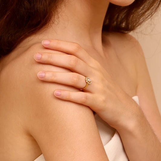 Close-up of a someone's hand on their shoulder wearing a gold ring with a diamond on a beige background