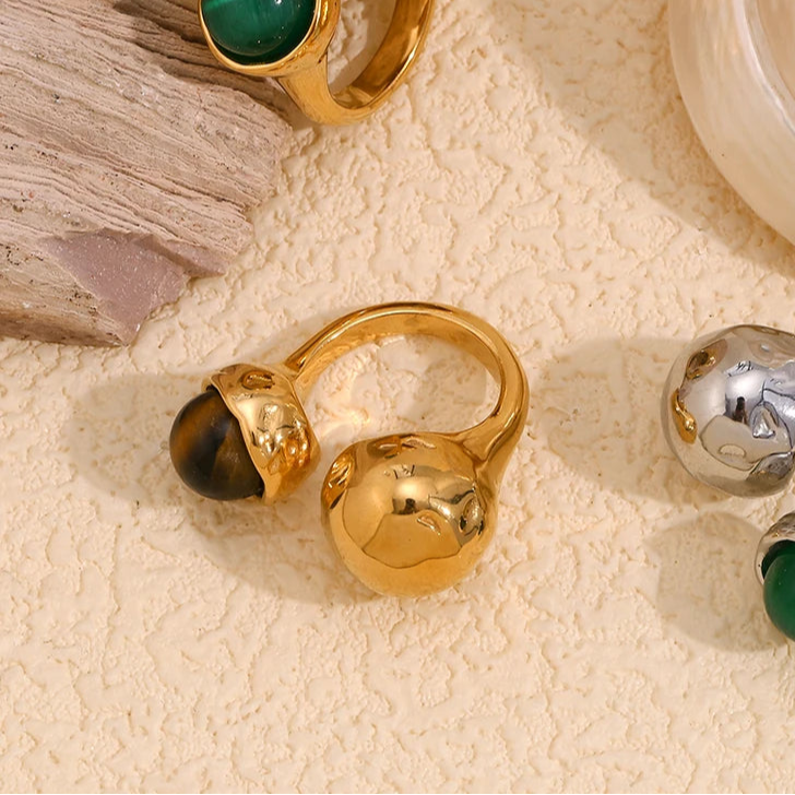 An 18K gold platted ring with a round tiger's eye stone on a hammer textured, asymmetrical band.